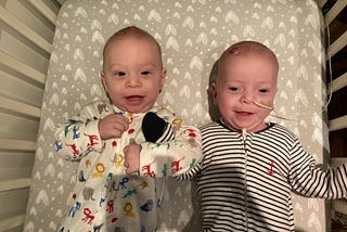 Joshua and Caleb laying side by side smiling at home in a crib