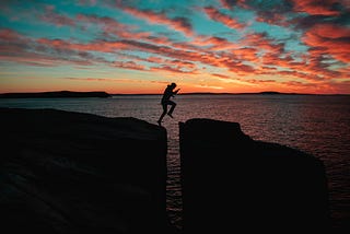 A runner leaps from one high rock to another, against the backdrop of the ocean.