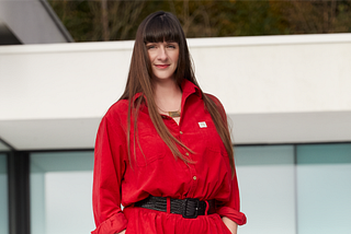 Laurens wears a red boiler suit in front of a beautiful whitebuilding