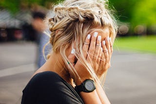 girl with blonde hair in braids around her head holding her hands over her face