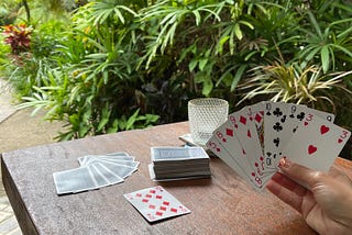 Playing cards on a wooden table against a tropical background, woman holding a hand of cards