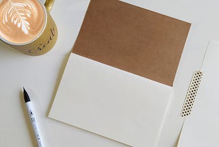 A brown notebook next to a coffee mug and a fountain pen