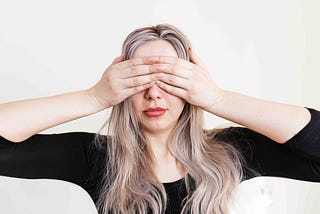 A woman covers her eyes gesturing “See no Evil”