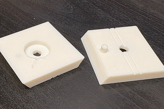 Photo showing a failed print of the revised mount on the left and a good one on the right (both printed with white PLA).