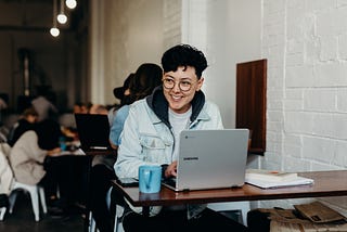 Woman sitting in front of an open laptop in a café, smiling