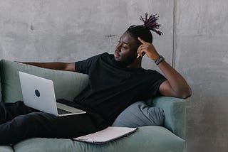 Image of a man laying on a couch working on his laptop