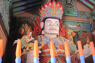 An ornate statue of a man inside a Buddhist temple, his crown is multicolored