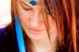 Young red-haired woman dressed in blue, looking down in contemplation.