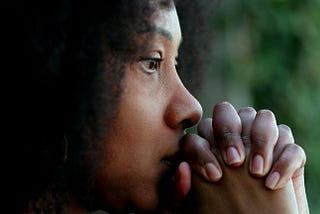 Close-up of a woman’s face with praying hands covering her mouth.