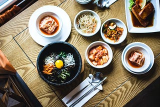 A view from the top of a dinning table with 7 different dishes of asian-fusion food.