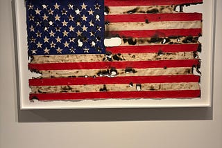 An acrylic painting of the American flag, framed, with dis-coloured lines and simulated burn marks.