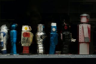 A variety of toy robots stand on a shelf.