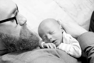 Joel holding his sleeping newborn son and looking down at him. In black and white.