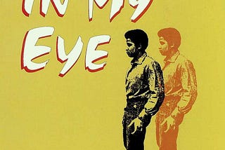 The book cover for Blood in My Eye is yellow, with the title letters in stylized white lettering with red accents. A black and white print image of a black man, standing and looking off, is featuring, with a duplicate, orange version of the same image superimposed to the right.