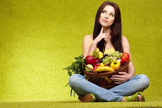 Pretty girl holding basket of fruit and vegetables, while contemplating something