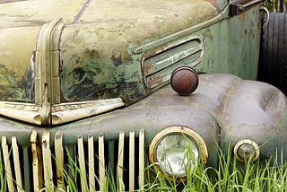 Front end of rusty vintage Ford truck sitting in a patch of weeds.