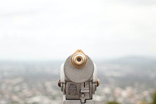 binoculars overlooking a view of a city from the top of a hill