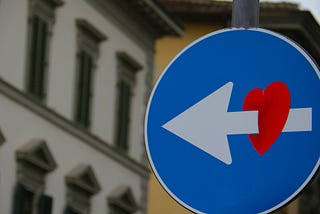 A one direction road sign with a heart sticker on the arrow