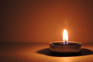 A single candle burning in darkness, its flame casting a soft, warm glow against a muted background, symbolizing quiet reflection, hope, and vigilance.