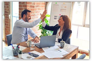 Professional colleagues high-fiving at a desk