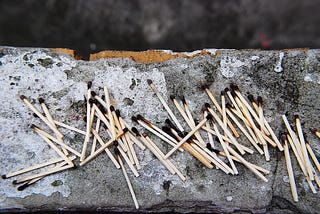 A pile of burnt-out matches on a piece of concrete.