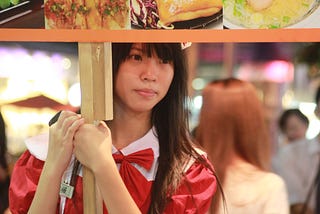 A lady with a sign promoting various stalls at the night market