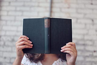Woman reading a book — face obscured by the book