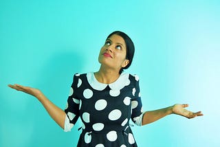 A girl in a polka dot dress looking up with her hands out in a questioning shrug