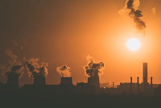 Large chimneys polluting the air during an orange sunset.