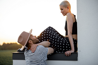 Young hip-looking couple talking. He’s in stylish hat and she has short cropped platinum blonde hair.