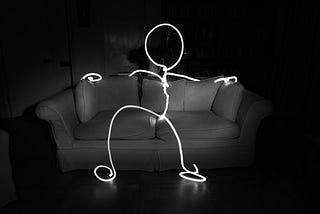 A faceless figure shaped out of wire sitting on a sofa