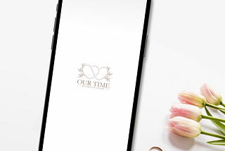 A mobile phone on the table showing the splash screens next to some tulips and two wedding rings