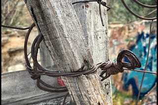 Rusted wire wrapped around two gray posts.