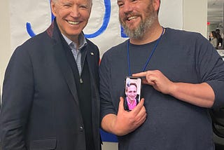 Joe Biden stands left of Dan Woods. Dan is holding his phone with Matt on the screen to meet the boss.