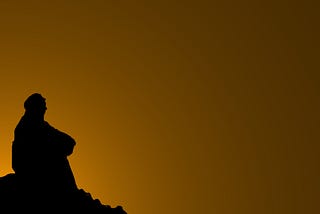 Photo showing the silhouette of a person sitting alone against a dark sky. It communicates a sense of sadness and isolation.