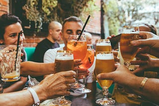 Glasses of beer and alcoholic drinks being clinked in a cheers at an outside table