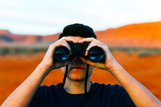 Photo of androgynous person looking through binoculars.