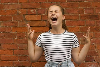 A young woman eyes closed, mouth open, hands in the air showing frustration