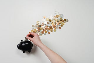 A black piggy bank with some coins. A hand is putting coins in it.