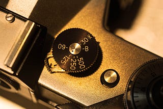 Close up monochrome photograph of the top plate of a camera showing the shutter speed selection dial.