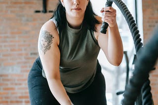 Plus sized lady doing battle ropes in a gym with an online personal trainer