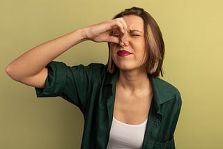 Attractive woman in green shirt holding her nose to avoid a stink.