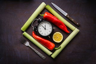 A square made of four pawpaw stocks, in which there are two chili peppers, a slice of orange, and a small clock