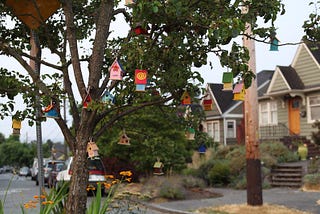 A cluster of small, colorful birdhouses in a tree in the foreground of a residential neighborhood.