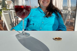 Picture of the author at a seaside restaurant with a rather large glass of red wine in front of her. She is smiling. I wonder why?