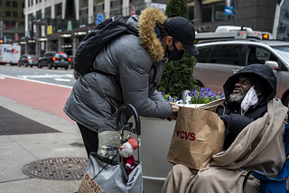 A passerby hands Anthony Lewis, a New Yorker experiencing homelessness, a bag filled with sandwiches and potato chips. (Photo: Hiram Alejandro Durán/THE CITY)