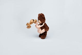 Teddy bear and Barbie figurines posed in a sex position on a solid gray background