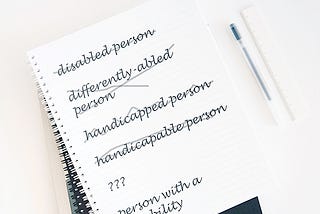 Notepad with the following phrases written on it: disabled person, differently-abled person, handicapped person, handicapable person, person with a disability. All phrases except person with a disability are crossed out.