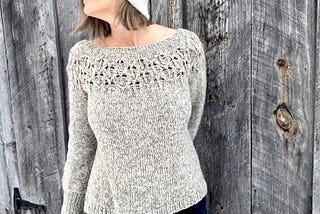 Woman wearing a hand-knit sweater, standing by a barn.