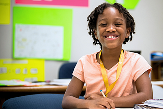 Image of a young Black student smiling while wearing a peach t-shirt ang yellow CTY lanyard.